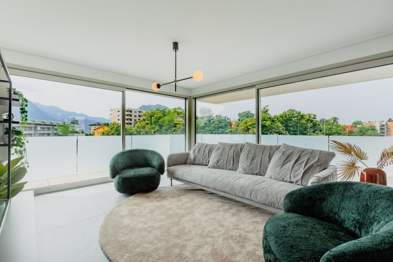 Ein modernes Wohnzimmer mit einer Couch, zwei Sesseln, einem runden Teppich und einer Deckenleuchte.