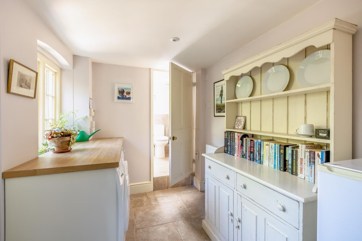 Una cocina con encimera de madera, un armario blanco con estantes y una puerta que da a otra habitación.