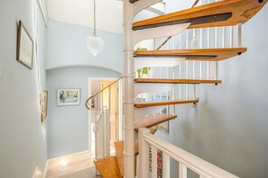 Eine Wendeltreppe mit Holzbodenstufen und weißen Geländern, hellblauen Wänden und einer hängenden Kristalllüster.