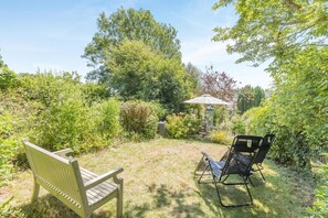 A garden with a bench and a chair, surrounded by lush greenery and trees. - 3 Bed in Bridport (oc-dc160) (Bothenhampton)