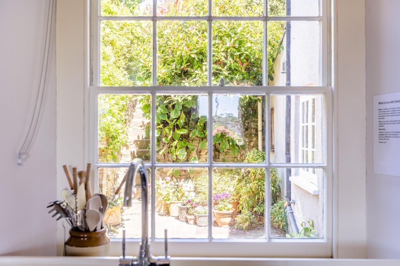 A window with a view of a garden, a sink, and a wall-mounted plaque.