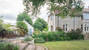 A stone house with a garden, a patio with chairs and an umbrella, and a circular stone feature. - 4 Bed in Wareham (oc-dc182) (West Lulworth)