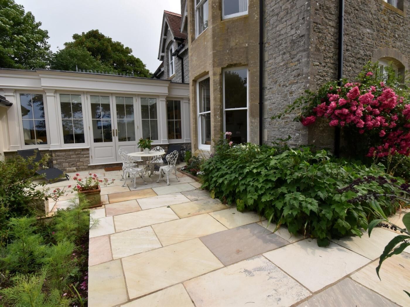 A patio with a stone floor, white chairs, and a table.