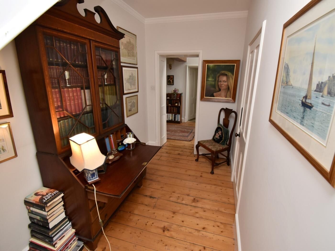 A hallway with a wooden floor, a desk with a lamp, a chair, and a bookshelf.