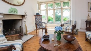 A room with a fireplace, a large mirror, a window with a view of greenery, and two upholstered chairs. - 4 Bed in Wareham (oc-dc182) (West Lulworth)