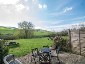 A patio with a table and chairs, a wooden fence, and a view of a grassy field and hills. - 2 Bed in Bridport (oc-dc162) (Chideock)