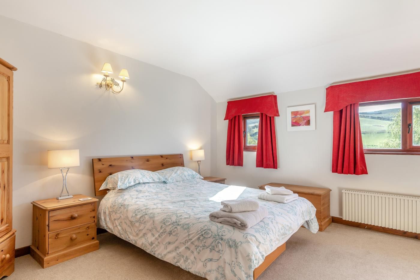 A bedroom with a bed, two bedside tables, a nightstand, a window with curtains, and a radiator.