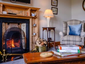 Ein gemütliches Zimmer mit Kamin, einem Karo-Sessel und einem Bücherstapel.