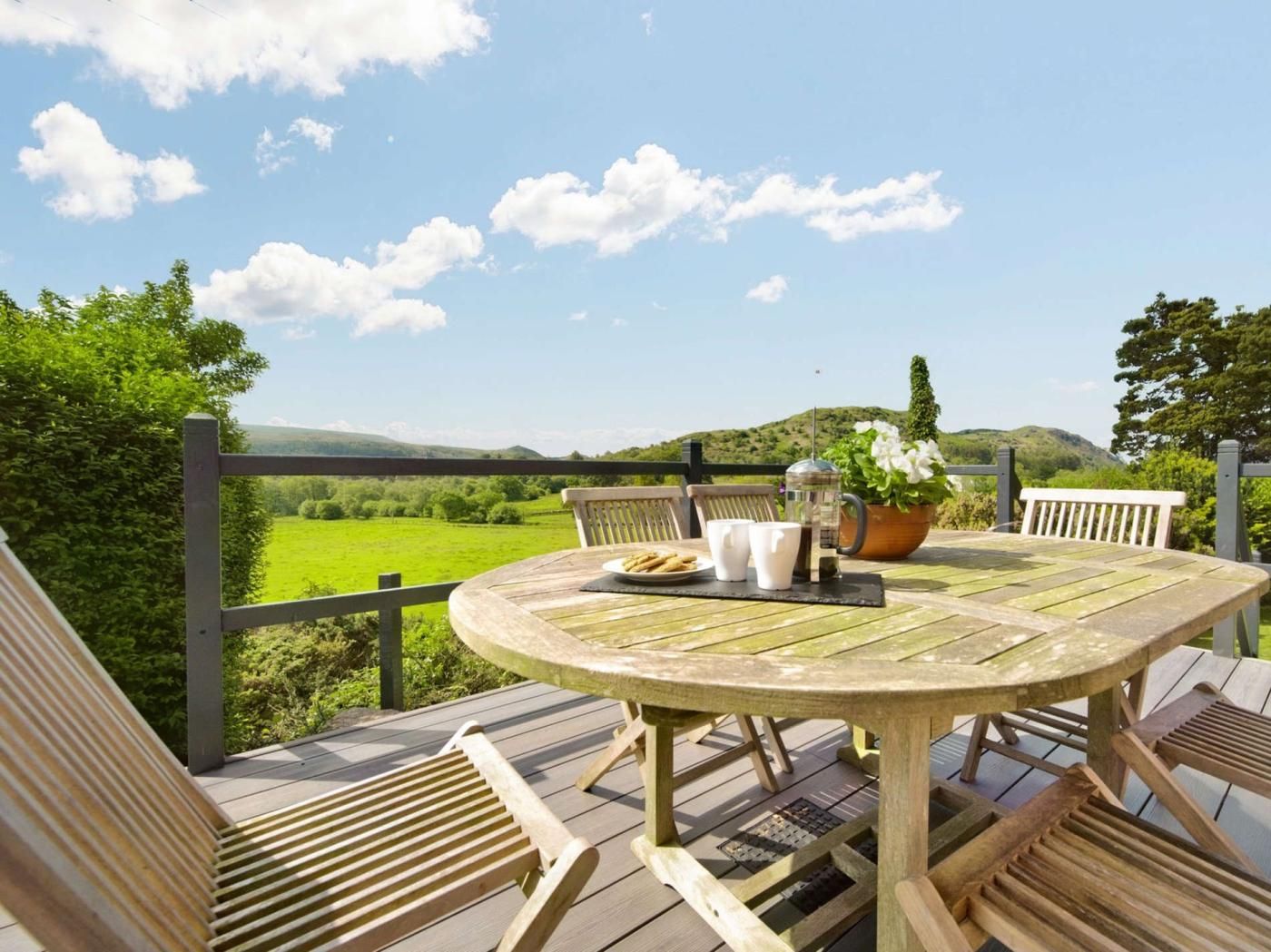 A wooden deck with a round table and chairs, a coffee pot, and a plate of biscuits.