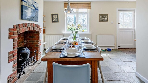 A dining area with a brick fireplace, a table set for four, and a window with a view of trees. - 4 Bed in Wareham (oc-dc204) (West Holme)