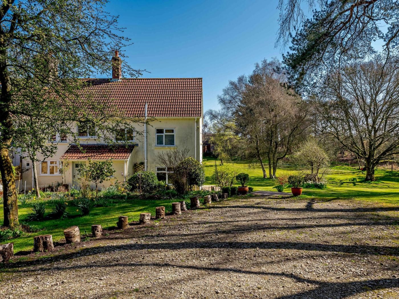 Ein zweistöckiges Haus mit rotem Ziegeldach, umgeben von einem gepflegten Garten mit verschiedenen Pflanzen und einem Kiesweg zum Eingang.