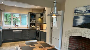 A modern kitchen with grey cabinets, a built-in oven, a white refrigerator, and a brick fireplace. - 4 Bed in Wareham (oc-dc204) (West Holme)