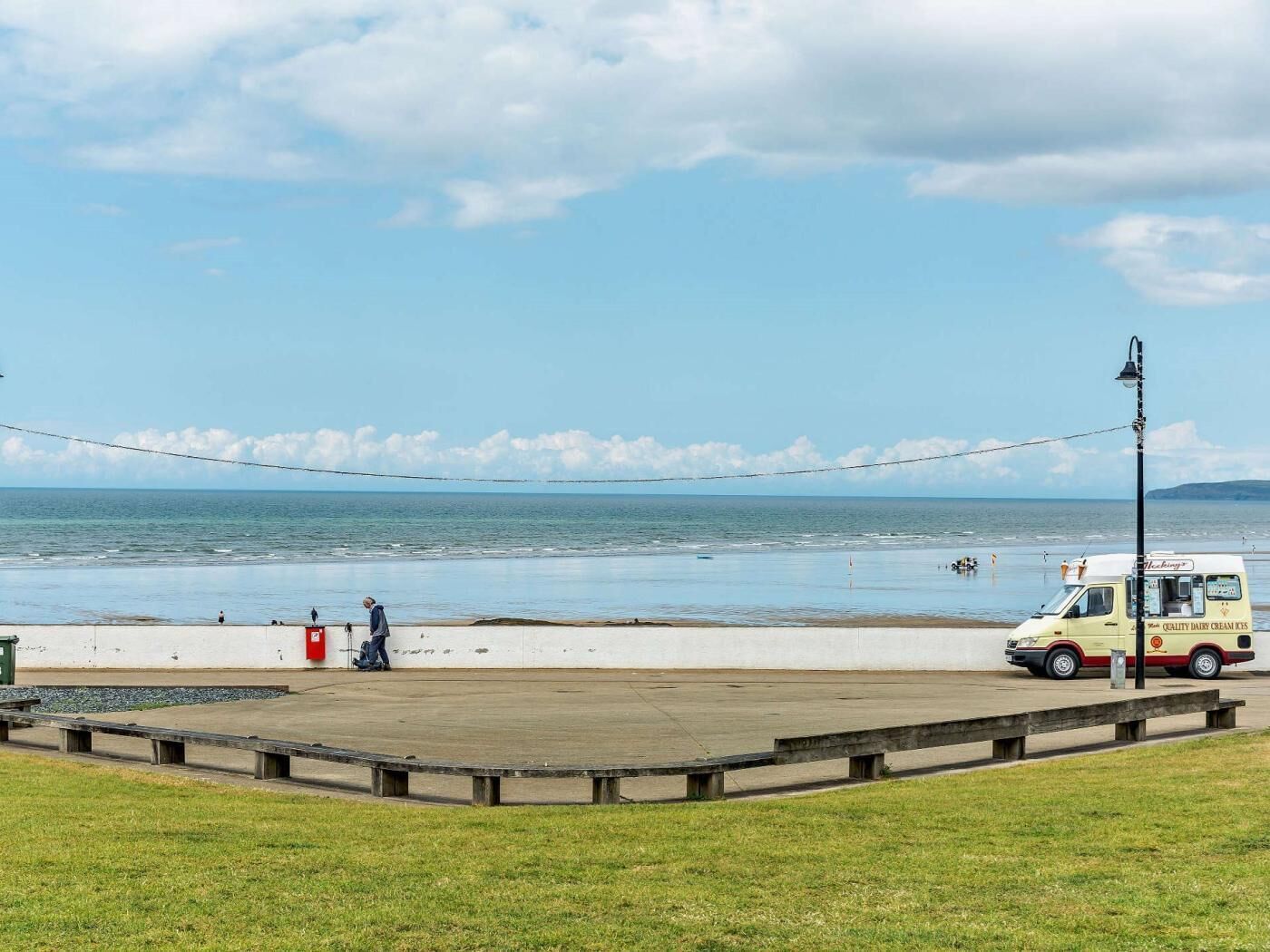 Une plage avec un camion de glaces garé, une promenade en béton et une zone herbeuse.