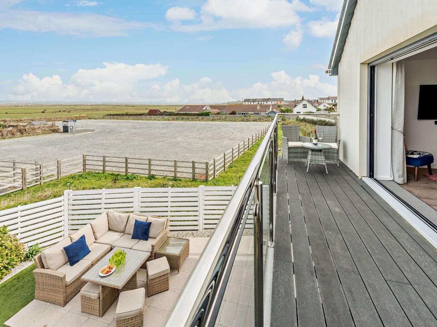 A balcony with outdoor furniture, a view of the beach, and a building in the background.
