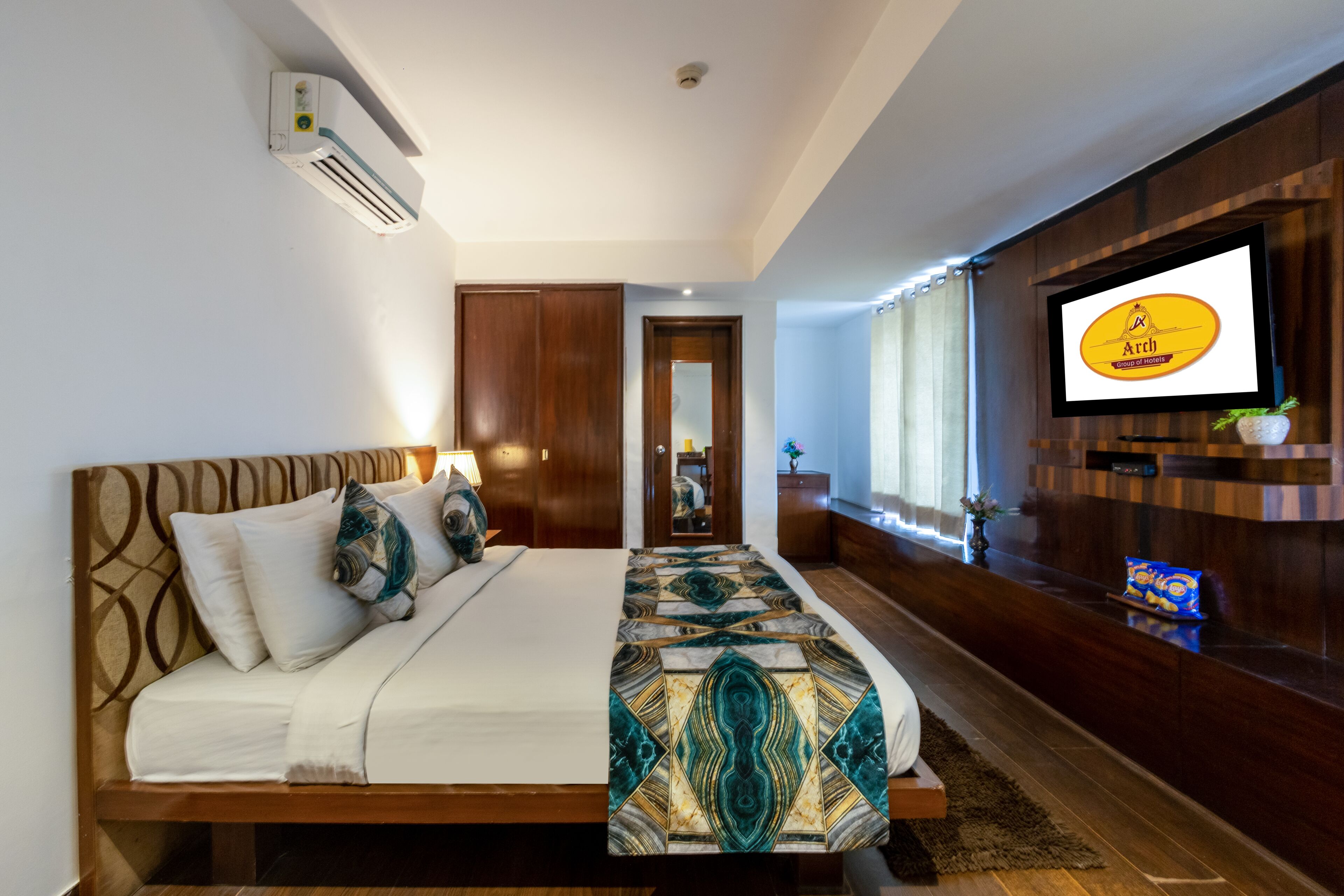 Una habitación de hotel con una cama grande, un televisor montado en la pared y un cabecero de madera.