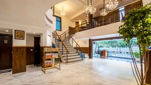 Um hall de hotel com piso de mármore, escada, lustres e balcão de recepção.