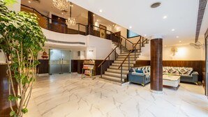 Um hall espaçoso com piso de mármore, escada, balcão de recepção e uma grande planta.
