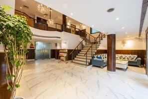 A spacious lobby with a marble floor, a staircase, a reception desk, and a large plant. - The Plaza Arch Premium - Del IGI Airport (New Delhi)