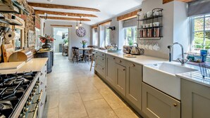 A modern kitchen with a central island, a dining area, and a view of the outdoors. - 4 Bed in Bridport (oc-dc212) (Burton Bradstock)