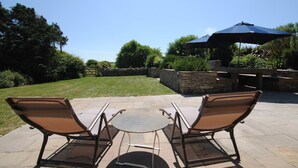An outdoor patio with two metal-framed chairs and a small round table, surrounded by stone walls and greenery. - 5 Bed in Swanage (oc-dc201) (Worth Matravers)