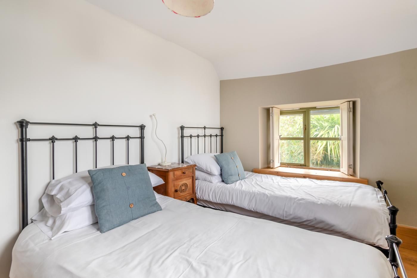 A bedroom with two beds, a nightstand, and a window with a view of greenery.
