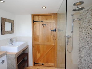 A bathroom with a wooden door, a shower, a sink, and a mirror. - 5 Bed in Swanage (oc-dc201) (Worth Matravers)