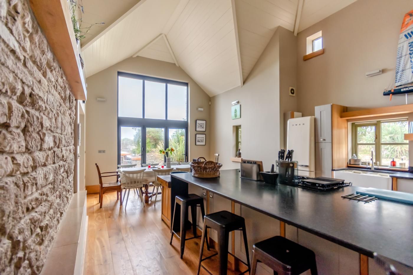 A kitchen with a large window, wooden flooring, and a stone wall.