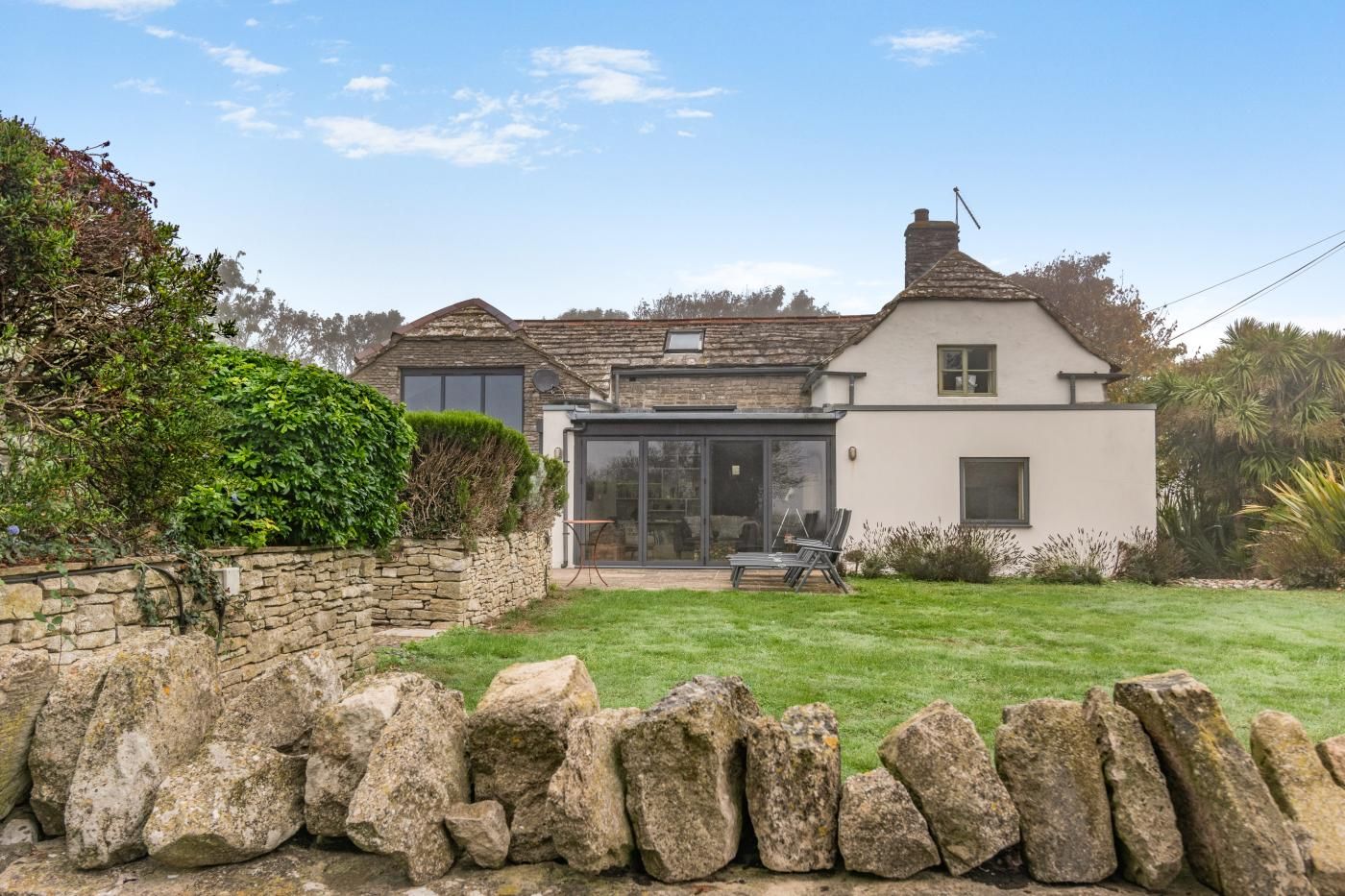 A two-story house with a stone wall, a glass conservatory, and a well-maintained lawn.