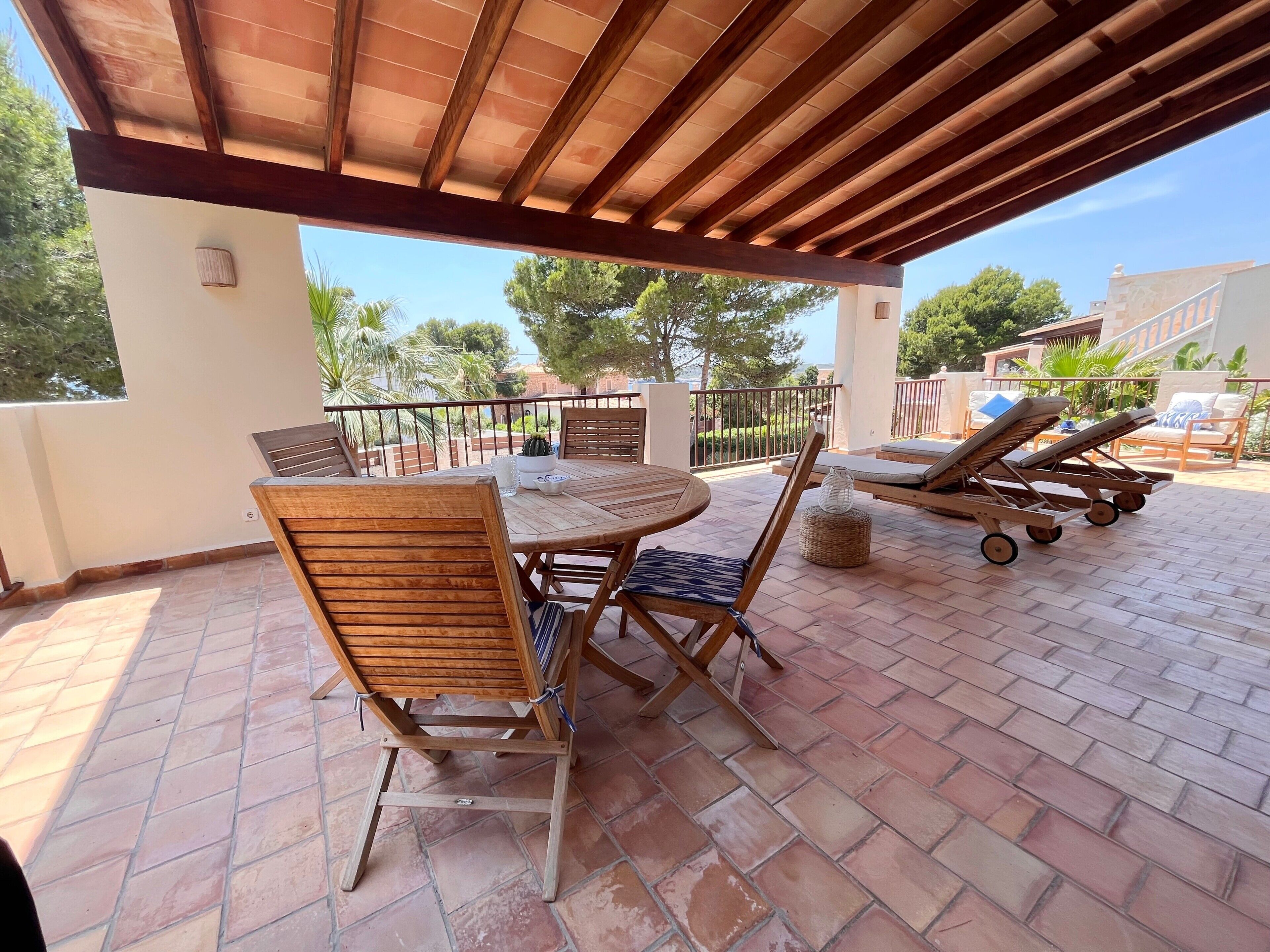 Un patio techado con mobiliario de madera, una mesa y sillones de descanso.