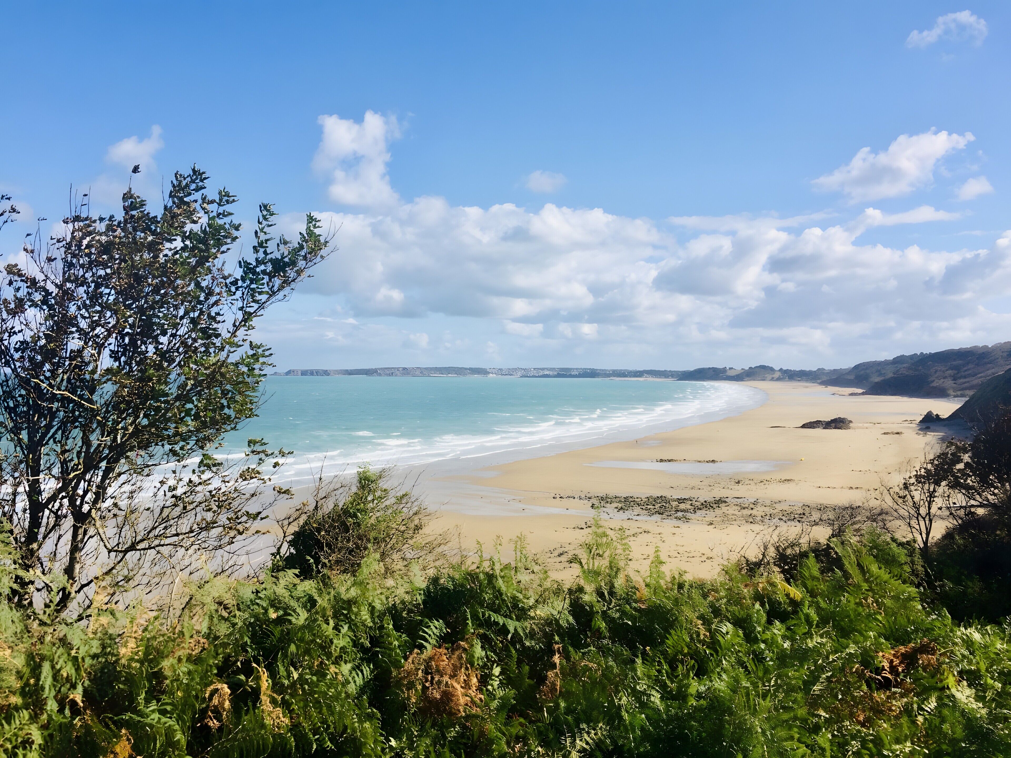 A coastal landscape with a sandy beach, a clear sky, and distant hills.