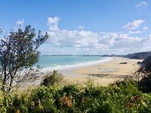 Un paisaje costero con una playa arenosa, cielo despejado y colinas lejanas.