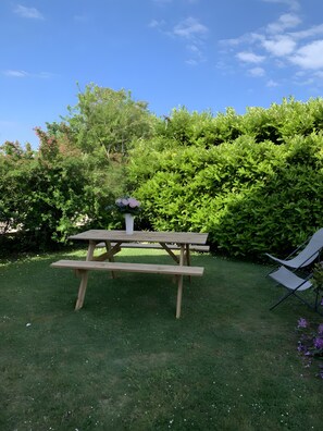 Una mesa de picnic de madera con bancos en una zona verde, con follaje denso al fondo.