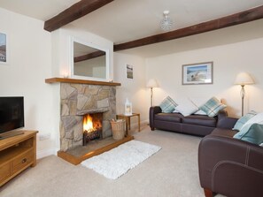 Ein Wohnzimmer mit Kamin aus Stein, einem Fernseher, einer Couch und einer Lampe.