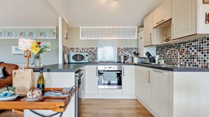 Una cocina compacta con armarios blancos, microondas, hervidor y cafetera.