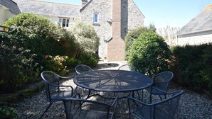 Ein Steinhaus mit Satteldach, umgeben von Grünflächen und einer Schotterterrasse mit Metallstühlen und einem runden Tisch.