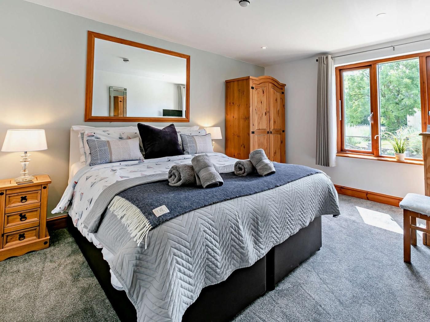 A bedroom with a bed, bedside tables, a wardrobe, a window with a view, and a mirror on the wall.