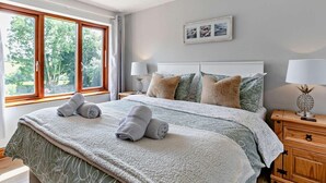A bedroom with a large bed, two bedside tables, a window with curtains, and a framed picture on the wall. - 6 Bed in Bideford (oc-75553) (Buckland Brewer)