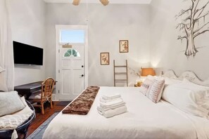 A bedroom with a bed, a desk, a chair, a TV, and artwork on the wall. - Relaxing Bohemian Villa w Heated Pool 5br 4ba (New Orleans)
