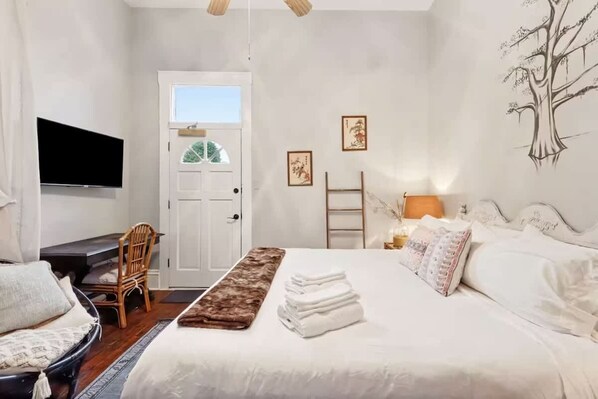 Une chambre à coucher avec un lit, un bureau, une chaise, un téléviseur et des œuvres d’art accrochées au mur.