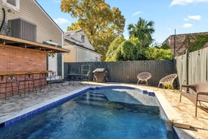 Un jardin avec une piscine, du mobilier de jardin et un espace barbecue.