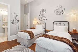 Quarto de hotel com duas camas, uma mesa de cabeceira, uma luminária e obras de arte nas paredes.