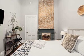 A bedroom with a bed, a fireplace, a white door, and a wall-mounted TV. - Relaxing Bohemian Villa w/ Heated Pool 5br 4ba (New Orleans)