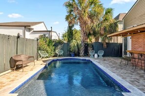 A backyard with a swimming pool, patio furniture, and a wooden fence. - Relaxing Bohemian Villa w/ Heated Pool 5br 4ba (New Orleans)