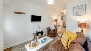 A living room with a flat-screen TV, a brown leather sofa, a coffee table with mugs, and a lamp. - 2 Bed in Brixham (oc-75550) (Brixham)