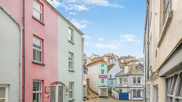 A narrow street with colorful buildings, a visible shop sign, and a staircase leading to a higher level. - 2 Bed in Brixham (oc-75550) (Brixham)
