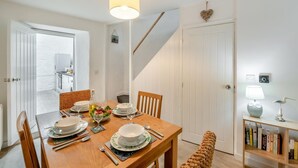 A dining area with a wooden table set for four, chairs, a hanging light fixture, a bookshelf with books, and a staircase leading to another room. - 2 Bed in Brixham (oc-75550) (Brixham)