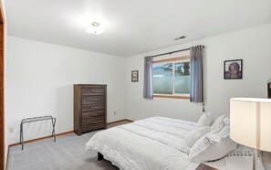 Un dormitorio con cama, cómoda, ventana con cortinas y una lámpara.