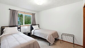 Ein Schlafzimmer mit zwei Einzelbetten, einem Fenster mit Vorhängen, einem Nachttisch mit Lampe und einer Heizung.