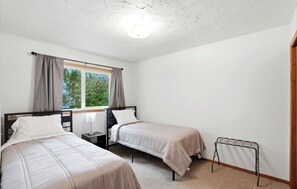 A bedroom with two single beds, a window with curtains, a bedside table with a lamp, and a radiator. - Amazing 4-bedroom house in Anchorage perfect for your next getaway. (Anchorage)