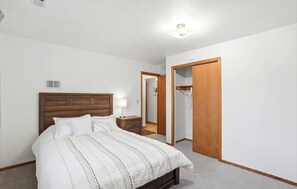 Ein Schlafzimmer mit hölzernem Kopfteil, einem Bett mit weißer Bettwäsche, einem Nachttisch, einer Lampe und einem Schrank mit Spiegel.